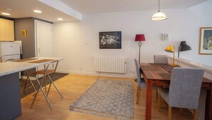 Une cuisine moderne dotée d’un réfrigérateur encastré, d’un coin repas avec une table et des chaises en bois, d’un lampadaire et d’un radiateur fixé au mur.