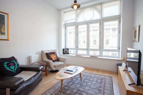 Una sala de estar con sofá, sillón, mesa de centro y televisor.