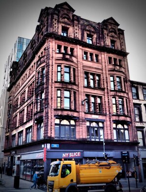 Ein mehrstöckiges Gebäude mit klassischer Architektur, das große Fenster und einen markanten Hauseingang an der Ecke zeigt.