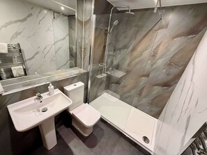 Une salle de bain moderne avec un mur en marbre, une douche à parois de verre, un lavabo blanc et des toilettes.