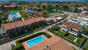 Zona residencial con un gran edificio que cuenta con piscina, paneles solares y cancha de tenis.
