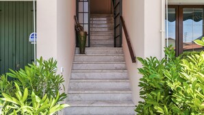 Una escalera conduce a la entrada de un edificio, bordeada por plantas verdes y una barandilla metálica.