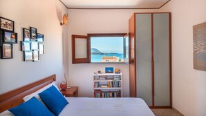 A bedroom with a bed, a bookshelf, a wardrobe, and a window with a view of the sea. - Terrazza Mandralisca by Wonderful Italy (Cefalù)
