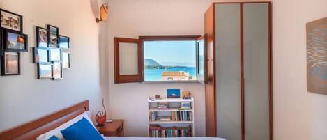 Quarto com cama, estante, guarda-roupa e janela com vista para o mar.