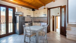 A kitchen with white cabinets, a stainless steel refrigerator, a dining table with metal chairs, and a wooden ceiling. - Terrazza Mandralisca by Wonderful Italy (Cefalù)