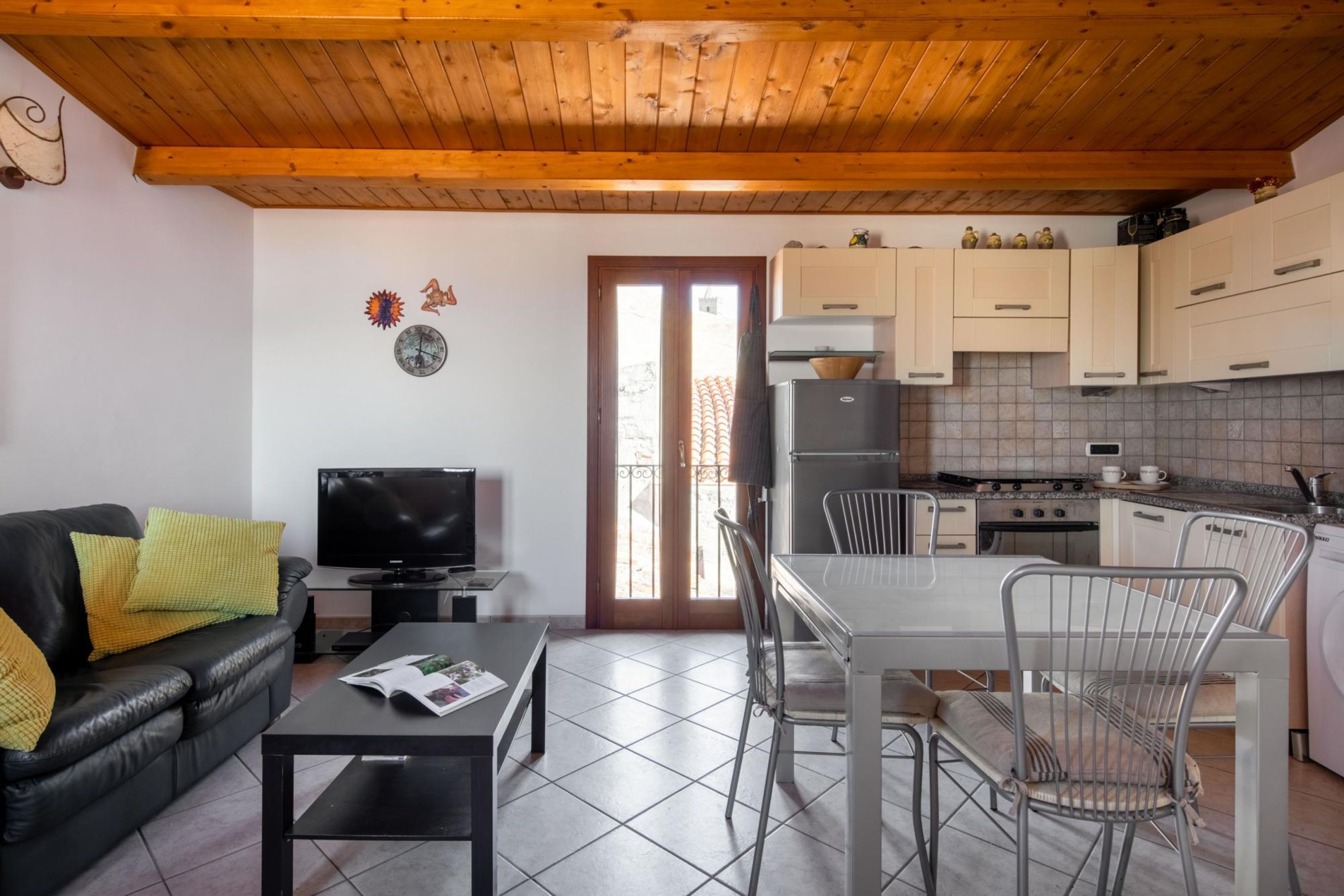 Un espace de vie compact comprenant un canapé, un téléviseur, une table à manger, des chaises, un coin cuisine et une porte donnant sur l’extérieur.