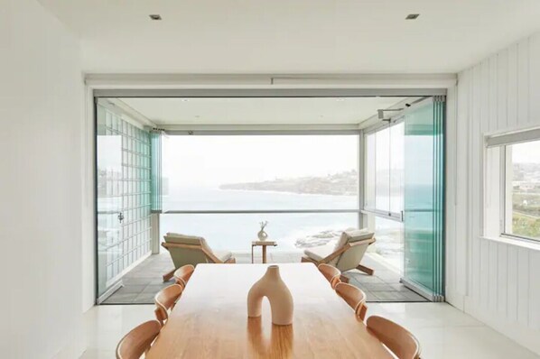 Un espace repas moderne avec une table et des chaises en bois, de grandes portes vitrées donnant sur un balcon avec vue sur la mer.