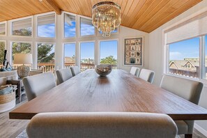 Enjoy meals with family and friends in this dining area with a long table and comfortable seating, offering a view of the surrounding landscape.