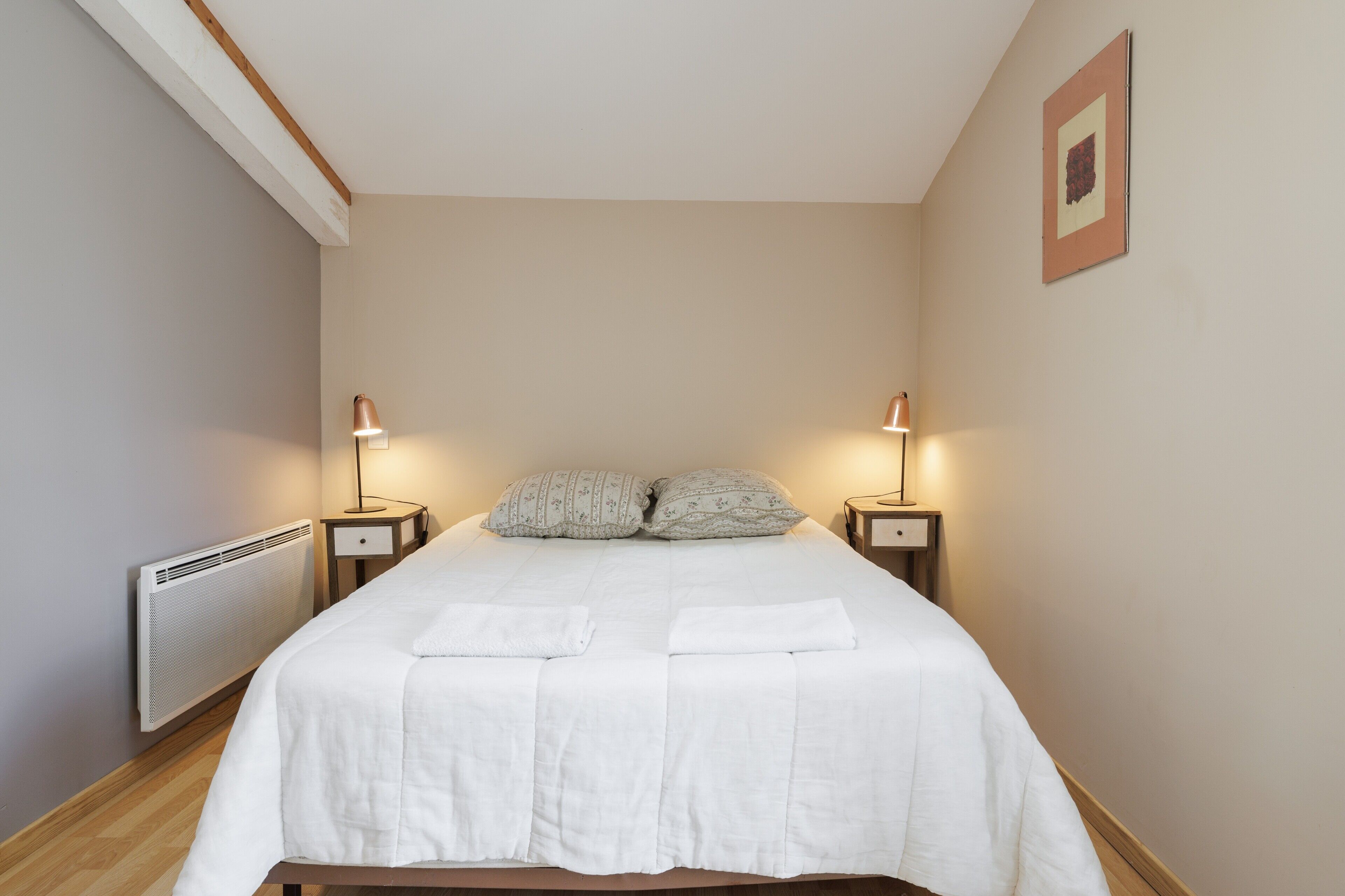 Een slaapkamer met een bed, twee nachtkastjes, een radiator en een foto aan de muur.