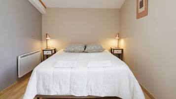 Een slaapkamer met een bed, twee nachtkastjes, een radiator en een foto aan de muur.