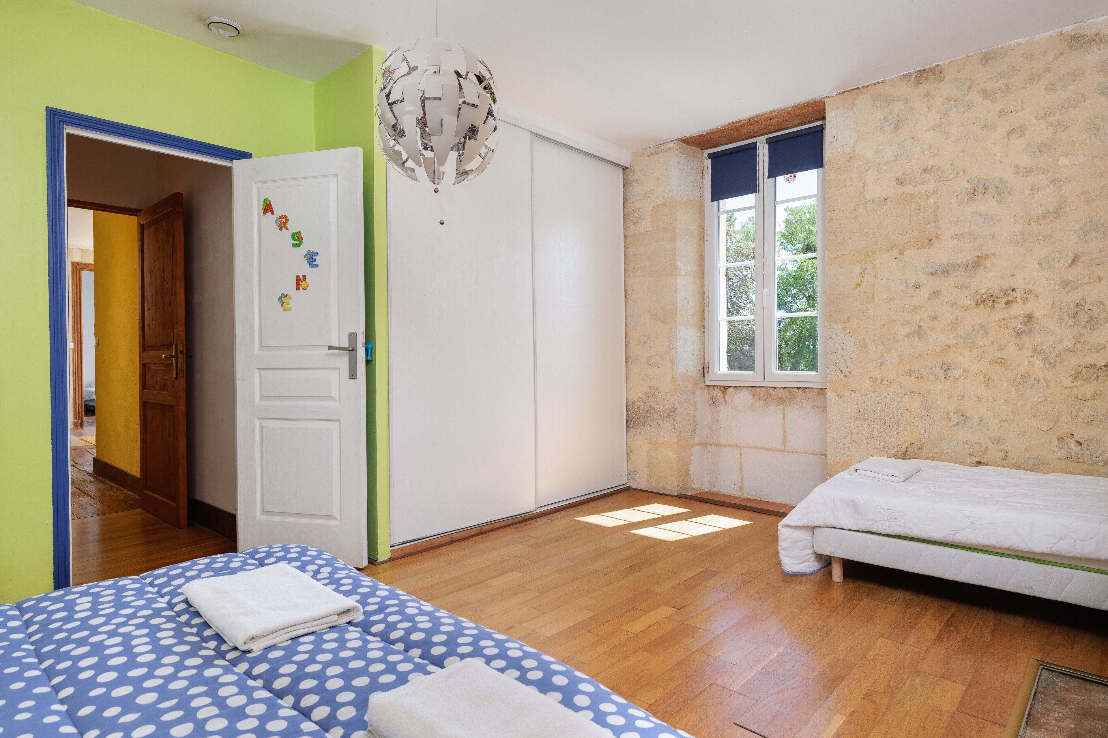 Quarto com cama, guarda-roupa, porta decorada com imãs de letras, janela e lustre.