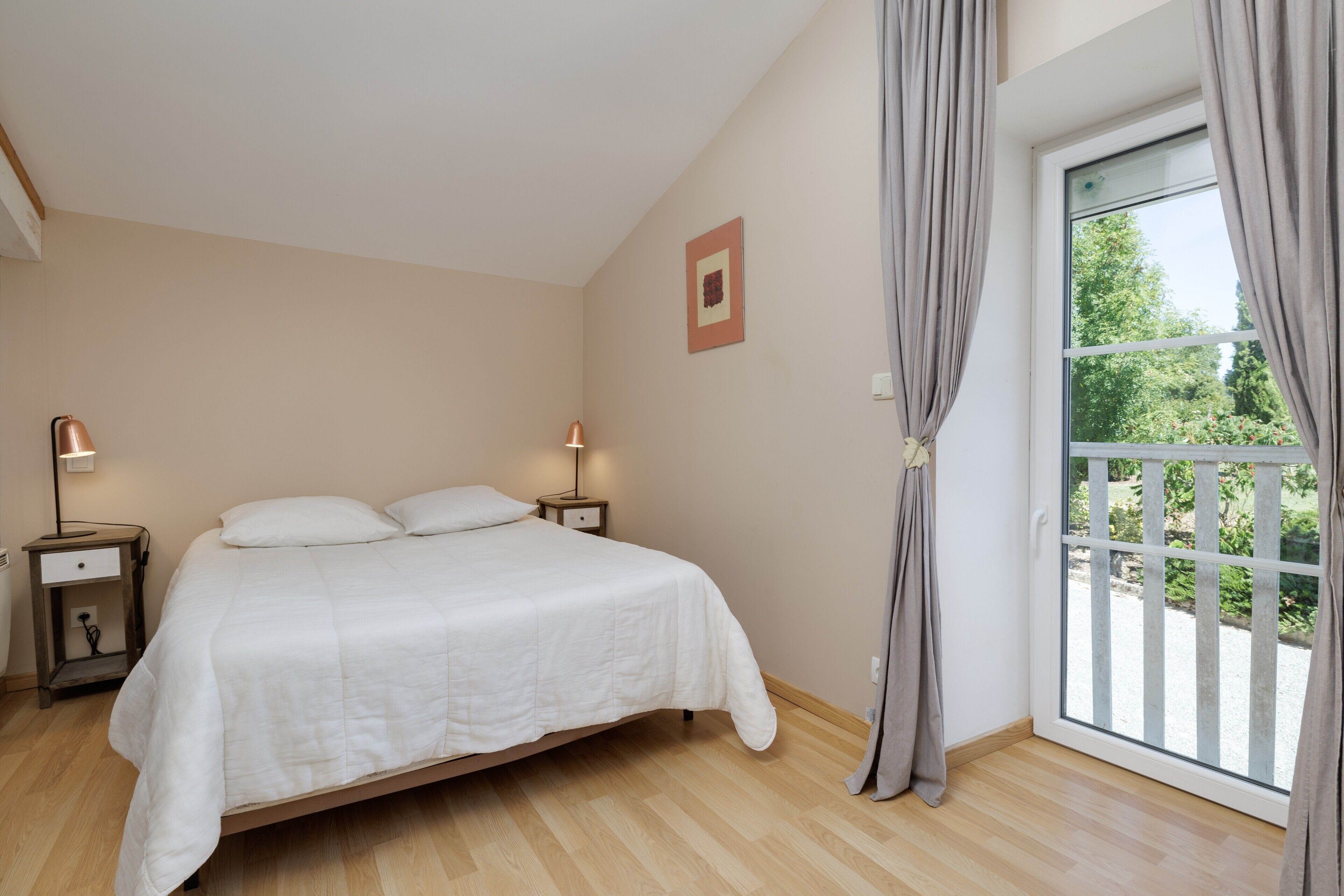 Un dormitorio con cama, mesitas de noche, una ventana con cortinas y vistas al exterior.