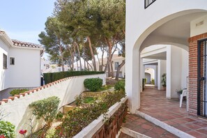 Une cour avec un mur blanc, une clôture en bois et un chemin dallé menant à l’entrée d’un bâtiment.