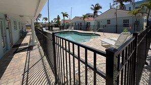 A pool area with a fenced deck, lounge chairs, and a building with a light blue exterior. - NEWLY RENOVATED Beach studio w/ pool view #4 (Treasure Island)