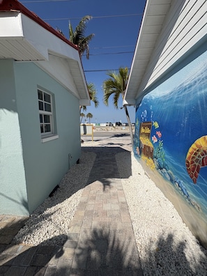 A pathway leading to a building with a mural of an underwater scene, palm trees, and a clear sky. - NEWLY RENOVATED Beach studio w/ pool view #4 (Treasure Island)