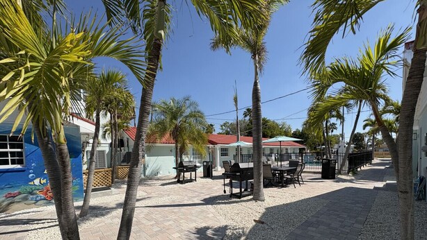 A paved outdoor area with palm trees, outdoor seating, and a building with a red roof. - NEWLY RENOVATED Beach studio w/ pool view #4 (Treasure Island)