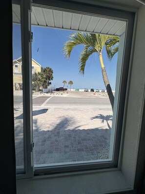 A view through a window of a paved area with palm trees, a parked car, and a building in the background. - Modern bungalow w/ Oceanview #9 (Treasure Island)