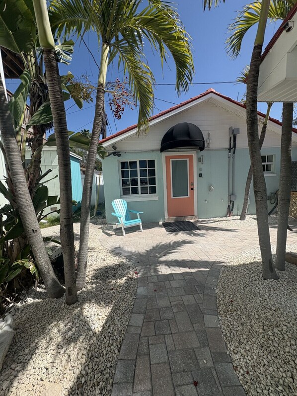A house with a red door, a blue chair outside, and palm trees around.