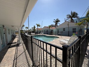 A pool area with a fenced deck, lounge chairs, and a building with a light blue exterior.