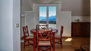 A dining area with a table and chairs, a view of mountains through a window, and a radiator on the wall.