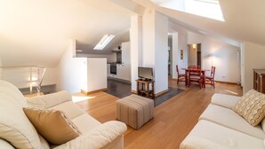 A spacious living area with a high ceiling, a dining table, and a kitchen in the background.