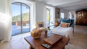 A spacious room with a large sliding glass door leading to an outdoor area, a bed with a white comforter, a wooden coffee table with a vase and remote control, and a view of a mountainous landscape. - Villa "Vue sur les Iles d'Or" with Sea View, Private Pool & Wi-Fi (Cavalaire-sur-Mer)