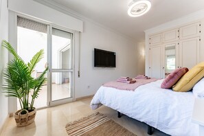 Une chambre à coucher comprenant un lit, un téléviseur, une plante en pot et une porte-fenêtre coulissante.