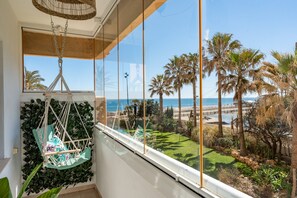 Een kamer met een groot raam dat uitkijkt op een strand, een hangstoel en uitzicht op palmbomen en de zee.