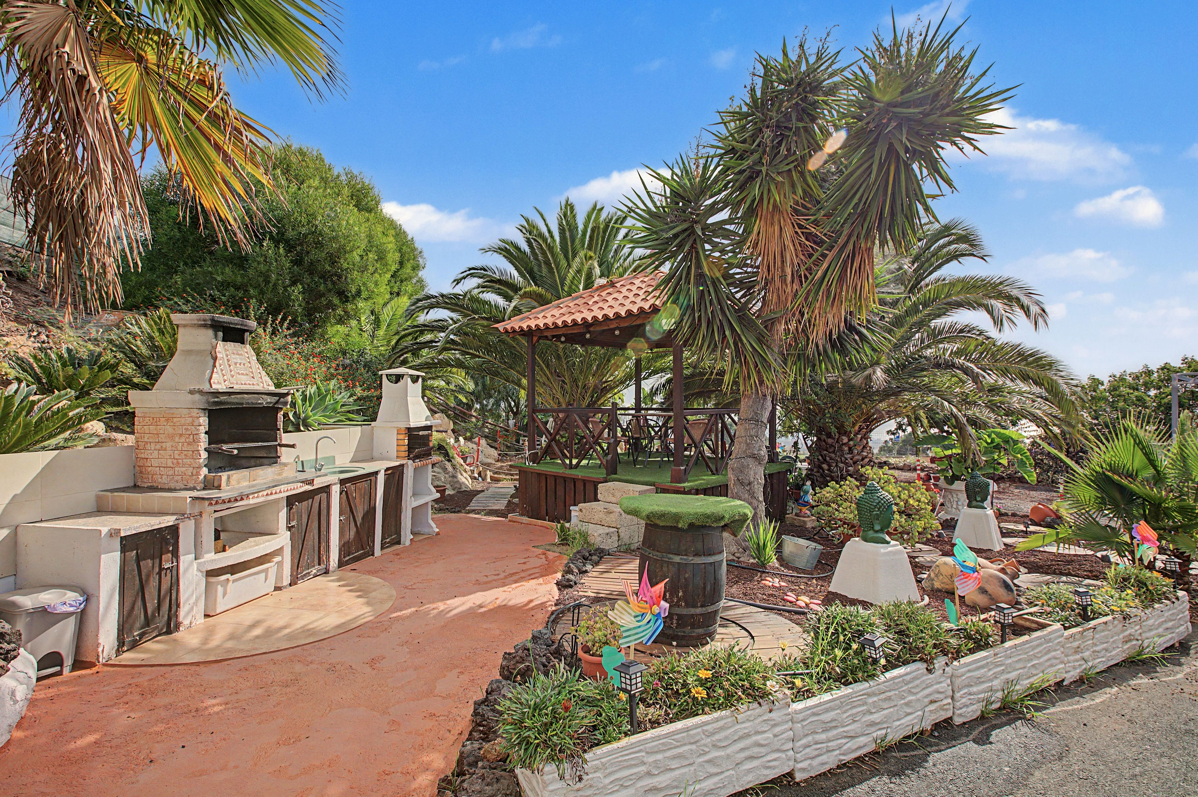 Un espacio patio con una parrilla de ladrillo, mobiliario exterior y una variedad de plantas y esculturas.