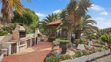 Un espacio patio con una parrilla de ladrillo, mobiliario exterior y una variedad de plantas y esculturas.
