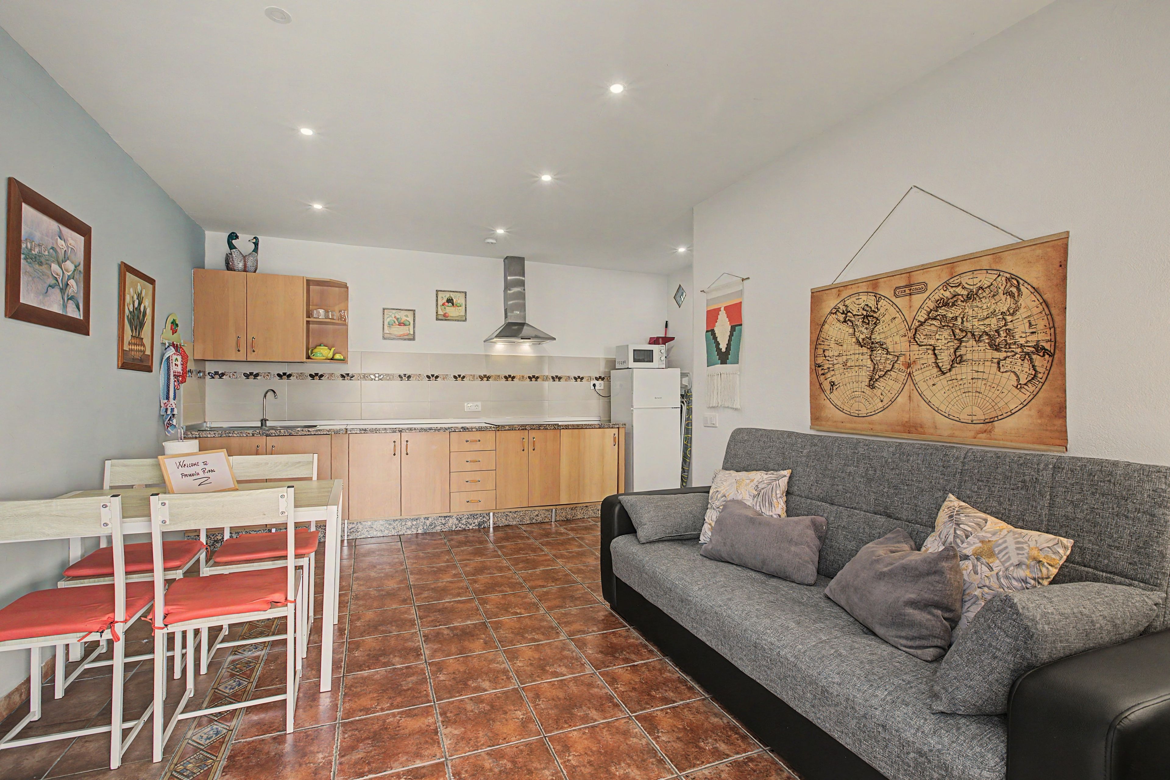 Um espaço de estar compacto com cozinha compacta, área de refeições com mesa e cadeiras, e sofá com almofadas.