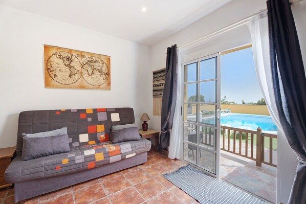 A room with a sofa, a world map artwork, a lamp, and a view of a swimming pool.