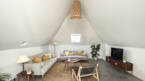 A loft-style living room with a high ceiling, a woven light fixture, a sofa set, a coffee table, a TV, and a plant. - Jasmine House Holiday Apartment with 2 Private Terraces & Wi-Fi (Tavira)