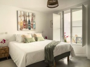 Une chambre à coucher comprenant un lit, une table de chevet, une œuvre d’art accrochée au mur et une grande fenêtre.