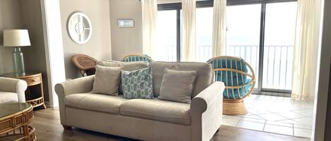 A living room with a beige sofa, wicker chairs, and a ceiling fan.