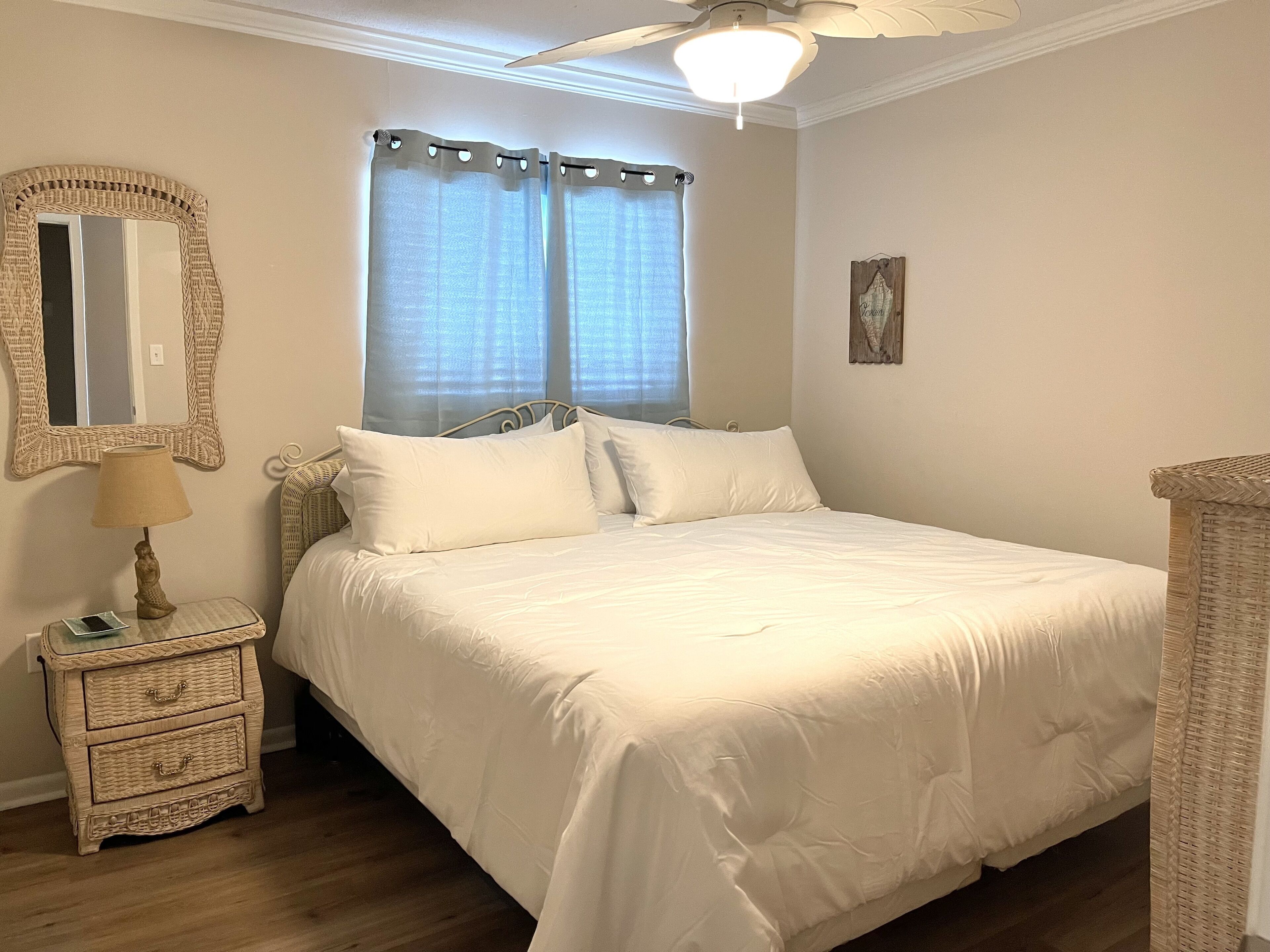 A neatly made bed with white bedding, a bedside table with a lamp, and a mirror on the wall.