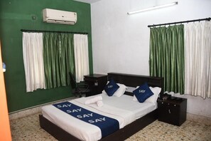 A hotel room with a bed, two nightstands, a chair, and a green wall. - Say Rooms Trip Manager Guest House (Bidhannagar)