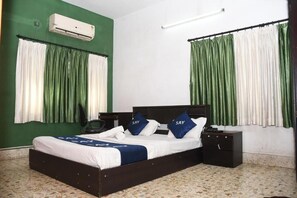 A bedroom with a bed, two bedside tables, an air conditioner, and green curtains. - Say Rooms Trip Manager Guest House (Bidhannagar)