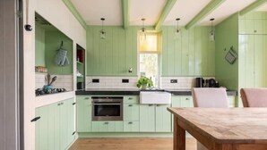 A kitchen with green cabinets, a wooden table, and a hanging light fixture. - Characteristic farmhouse on the dike (Andijk)