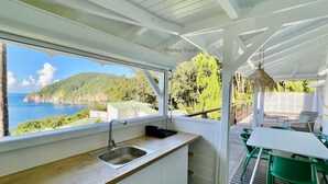 Una cocina con vista al mar, un comedor con sillas verdes y una terraza de madera.