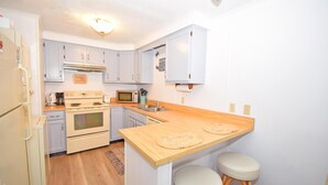 A compact kitchen with white cabinets, a microwave, a stove, and a wooden countertop. - Old Wharf 15 1 Bedroom Condo by RedAwning (Ocean City)