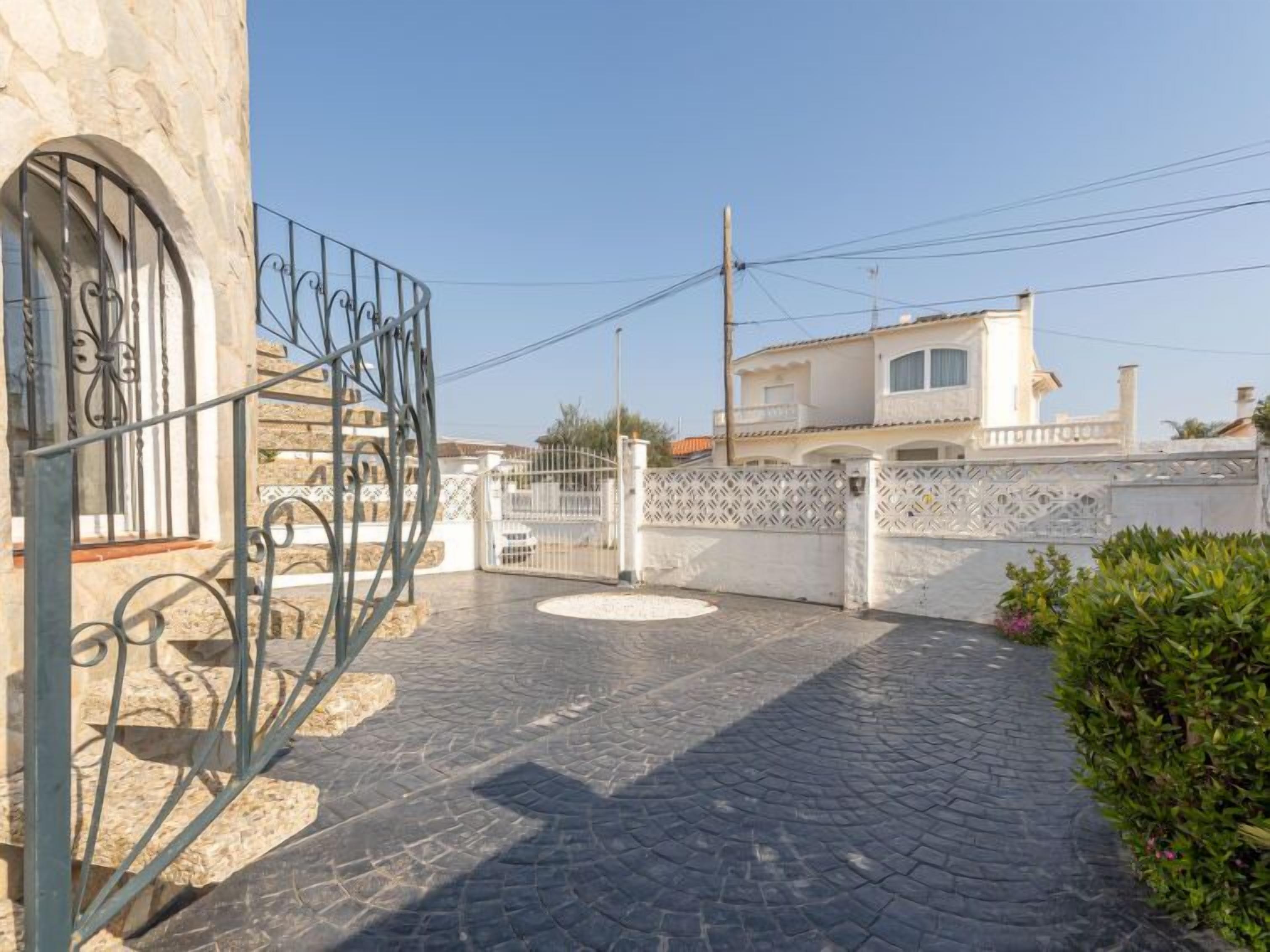 Un patio empedrado con una reja metálica decorativa, un edificio de piedra y una cerca blanca.