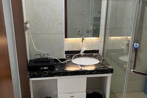 A modern bathroom with a marble countertop, a sink, and a glass shower enclosure. - Hongfuxuan Hotel (Jurong)
