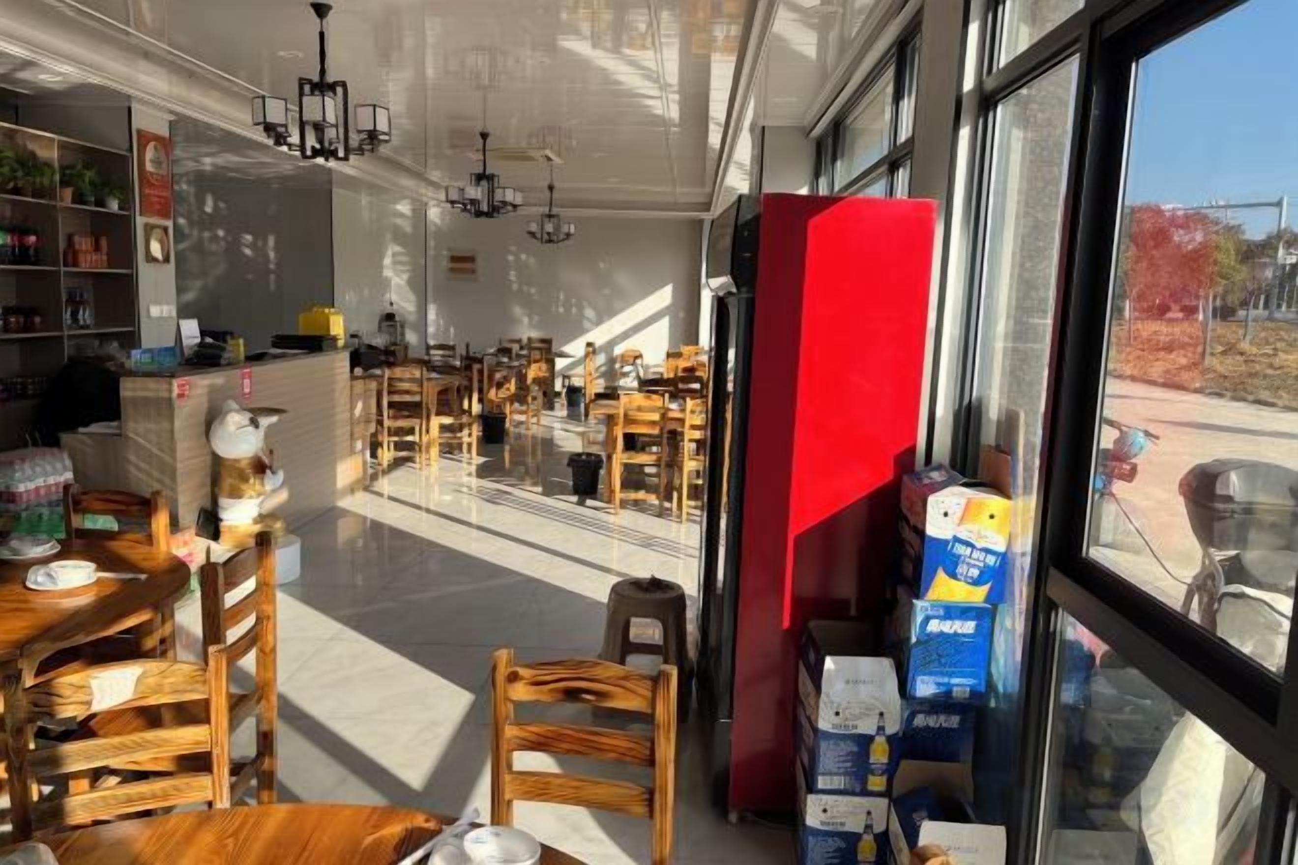 Un restaurante con mesas y sillas de madera, un mostrador rojo y vistas a través de la ventana.