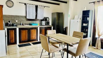 Une cuisine équipée d’une table à manger, de chaises, d’un réfrigérateur, d’un four à micro-ondes et d’une horloge murale.