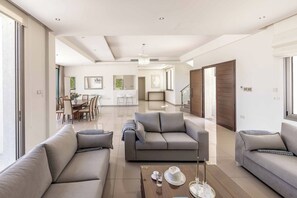 A spacious living room with a sofa, coffee table, and a dining area in the background. - Limni Beach Villa - Four Bedroom Villa, Sleeps 8 (Polis)