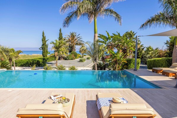 A pool with lounge chairs, palm trees, and a view of the ocean. - Limni Beach Villa - Four Bedroom Villa, Sleeps 8 (Polis)