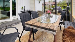 Eine moderne Terrasse mit einem Glastisch, schwarzen Stühlen und Blick auf den Garten.