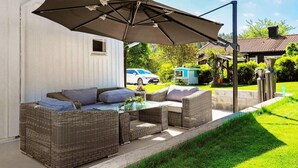Eine Terrasse mit Korbmöbeln, einem Tisch und einem großen Sonnenschirm.