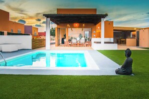 A modern outdoor pool area with a Buddha statue, a covered seating area, and a clear sky.
